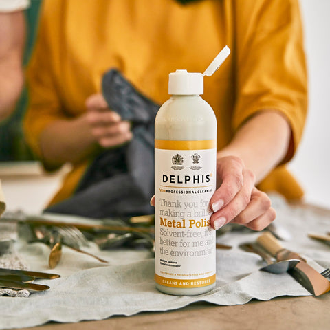 A person holding Metal Polish on a worktop whilst polishing cutlery